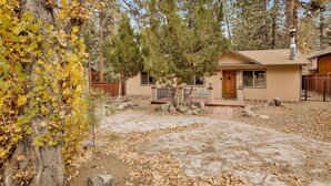 A cabin with a stone patio, surrounded by trees and a wooden fence. - Popko's Place #1426 (Big Bear Lake)