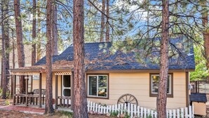 A cabin with a porch, a wheelbarrow, and a white picket fence.