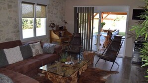 A living room with a brown sofa, a glass coffee table, and a leather ottoman. There is a sliding glass door leading to an outdoor patio area. - Le Refuge des Epicuriens (EYMET)
