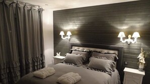 A bedroom with a dark wood headboard, two bedside lamps, a nightstand with a vase, and a bed with pillows and folded towels. - Le Refuge des Epicuriens (EYMET)