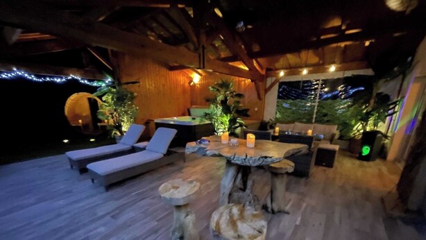An outdoor lounge area with wooden flooring, lounge chairs, a wooden table with candles, and potted plants. - Le Refuge des Epicuriens (EYMET)