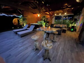 An outdoor lounge area with wooden flooring, lounge chairs, a wooden table with candles, and potted plants. - Le Refuge des Épicuriens - Cottage for 4, private hot tub, sauna, heated pool (EYMET)