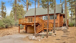 A wooden cabin with a balcony, a garage, and a stone foundation. - Living Log Cabin#1494 (Big Bear City)