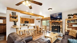 A rustic interior with a stone fireplace, wooden furniture, and a bar area. - Living Log Cabin#1494 (Big Bear City)