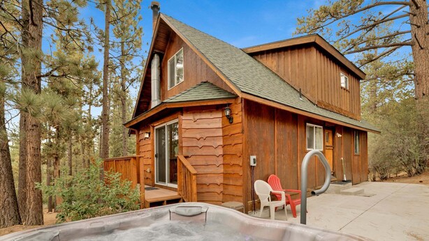 A wooden cabin with a hot tub, surrounded by trees. - Living Log Cabin#1494 (Big Bear City)