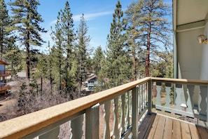A wooden deck with a railing overlooking a forested area with tall pine trees. - Midnight Howl #1536 (Big Bear Lake)
