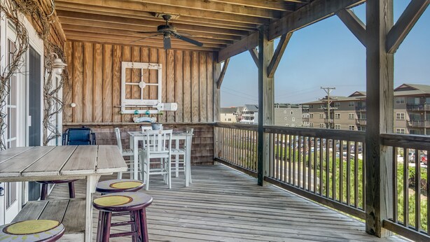 A wooden deck with a table and chairs, a ceiling fan, and a view of surrounding buildings. - T's Retreat: Semi-oceanfront, third floor condo, two beach accesses close by. (Kill Devil Hills)