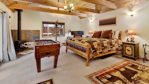 Een gezellige slaapkamer met een houten plafond, een bed met quilt, een tafelvoetbaltafel, een open haard en een raam met uitzicht.