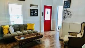 Un salon avec un canapé, une table basse en osier, une porte rouge et un vélo accroché au mur.