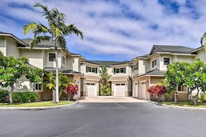 Una calle residencial con casas de dos pisos, cada una con un garaje, rodeada de céspedes bien cuidados y palmeras.