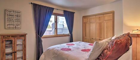 Un dormitorio con cama, armario de madera, aparador y ventana con cortinas.