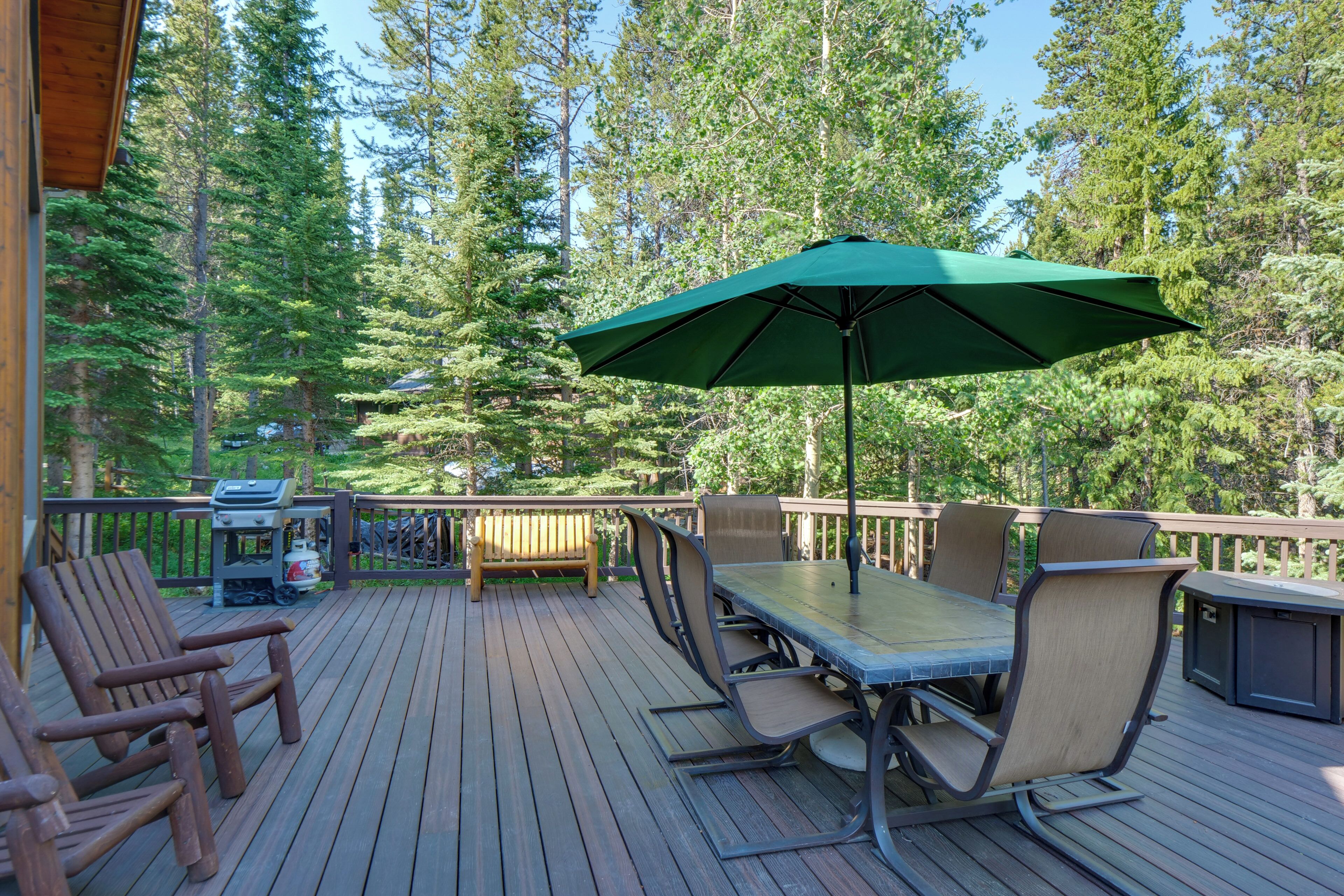 Une terrasse en bois avec des meubles d’extérieur, un barbecue et un parasol vert.