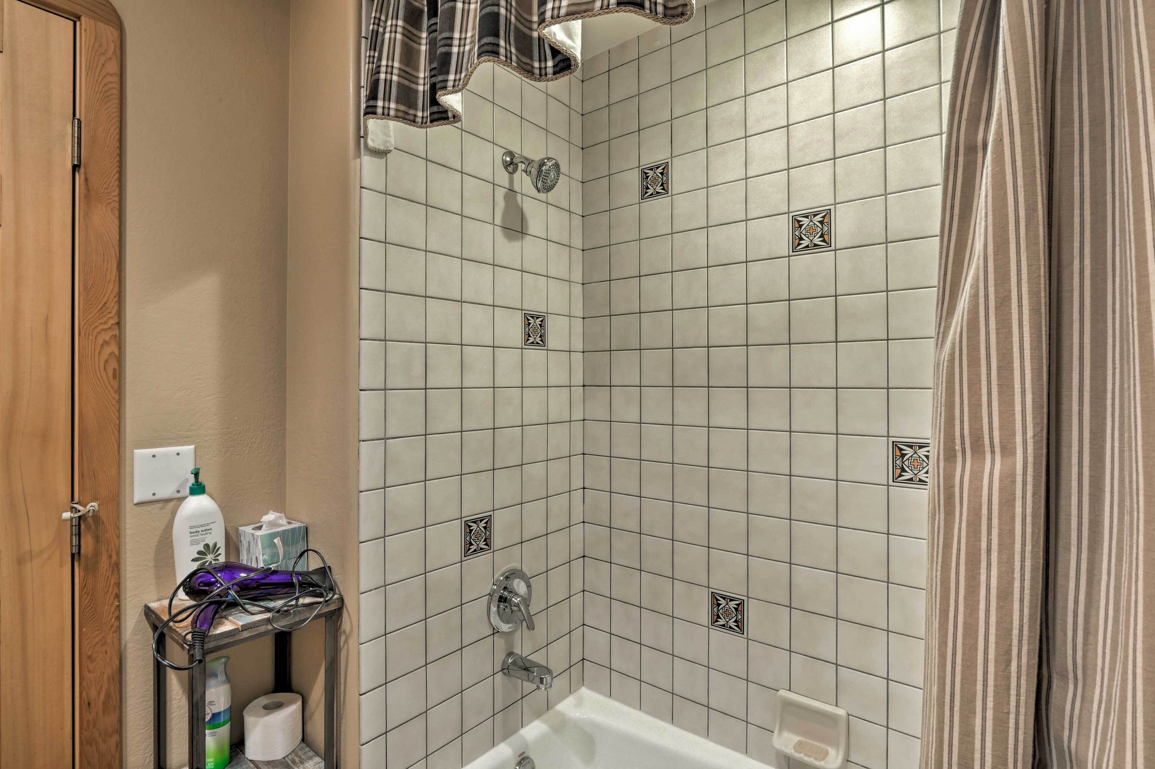 A bathroom with a shower, a toilet, and a sink. There is a towel rack with a towel and a bottle of shampoo.