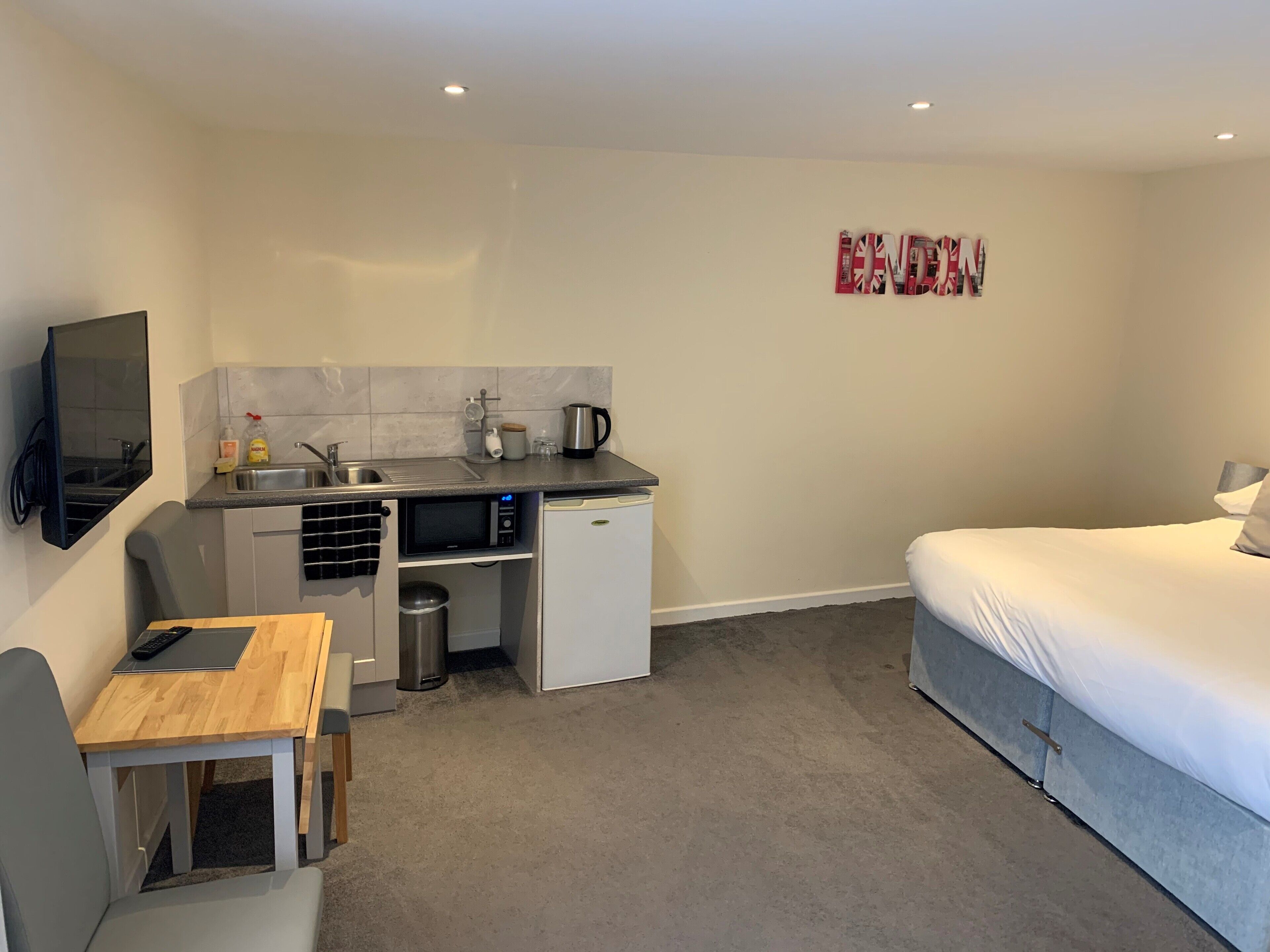 A compact hotel room with a kitchenette, a bed, and a small table with a chair.