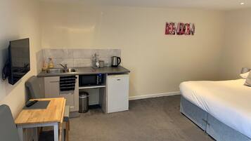 A compact hotel room with a kitchenette, a bed, and a small table with a chair.