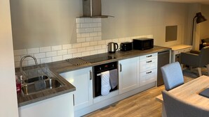 A modern kitchen with white cabinets, a stainless steel sink, a microwave, a toaster, and a kettle. - Fornham Guest House (Chertsey)