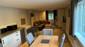 A modern kitchen with a microwave, toaster, and cabinets. There is a dining area with a table and chairs. - Fornham Guest House (Chertsey)