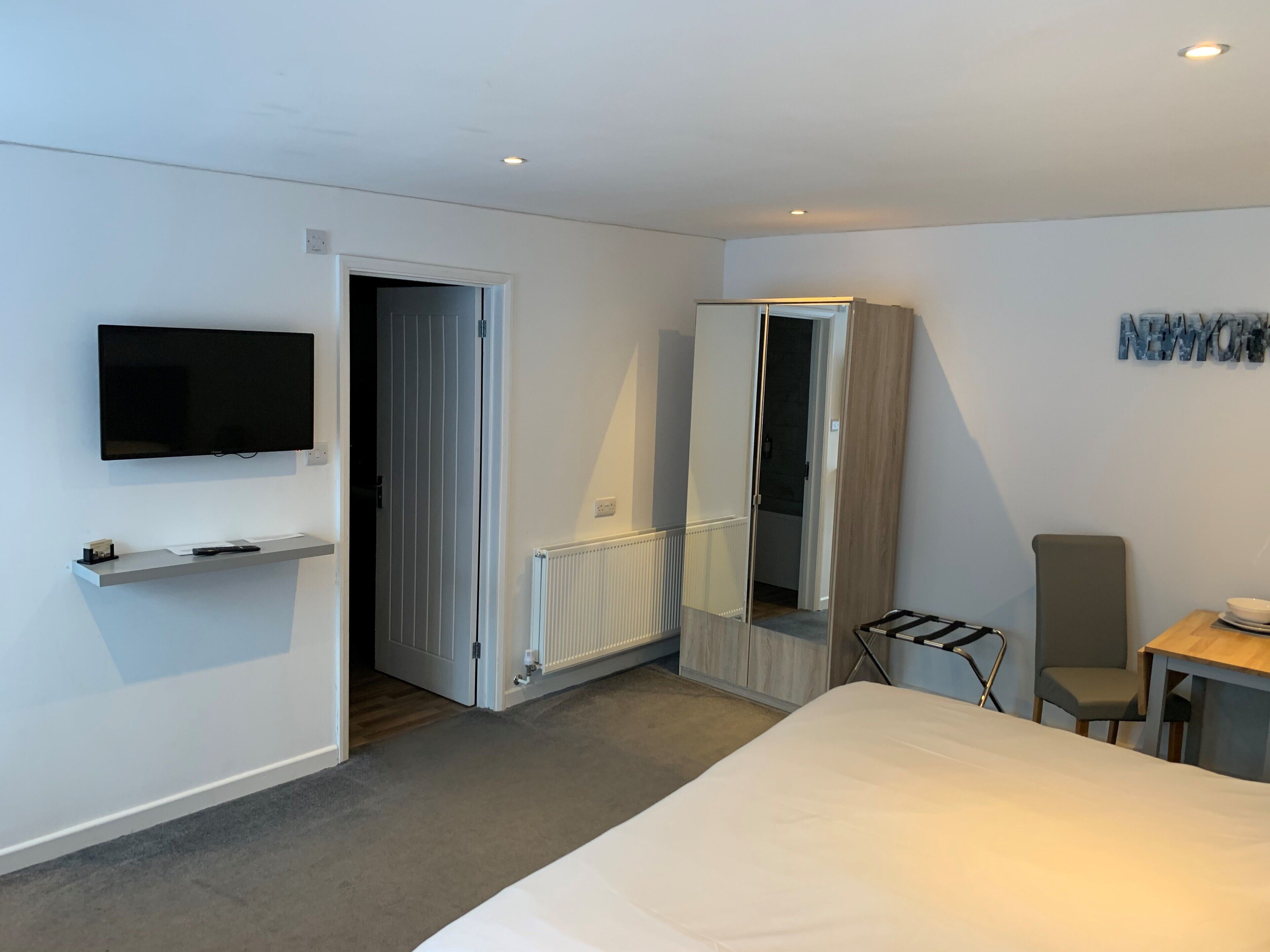 Una habitación de hotel moderna con una cama, un televisor montado en la pared, un escritorio con una silla y un armario.