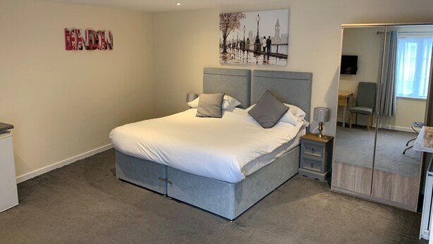 A modern bedroom with a large bed, bedside tables, a desk, and a mirror. - Fornham Guest House (Chertsey)