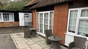 A patio with wicker furniture, a glass table, and a brick building with large windows. - Fornham Guest House (Chertsey)