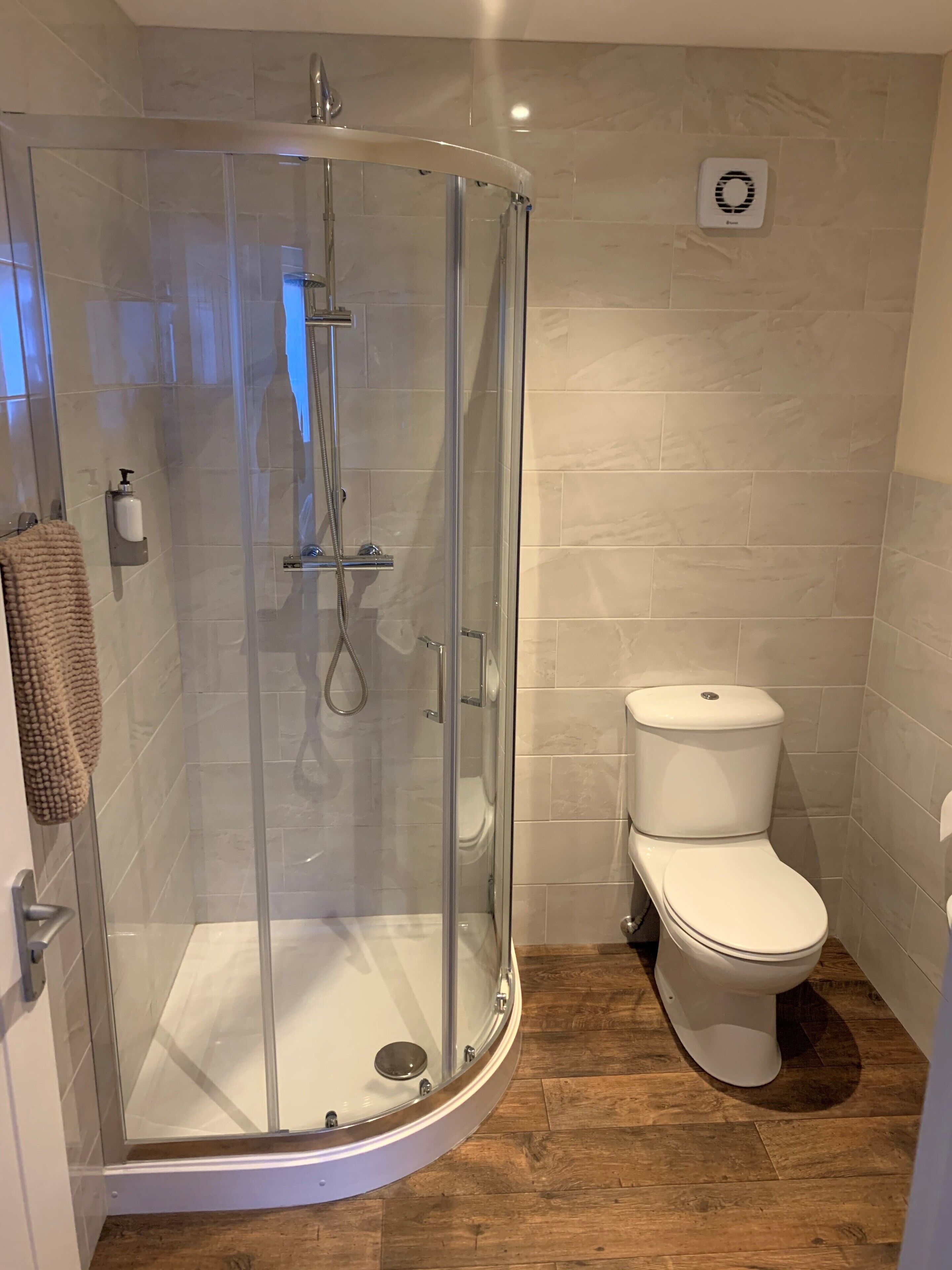 A modern bathroom with a glass-enclosed shower, a toilet, and a wooden floor.