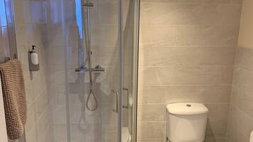 A modern bathroom with a glass-enclosed shower, a toilet, and a wooden floor.