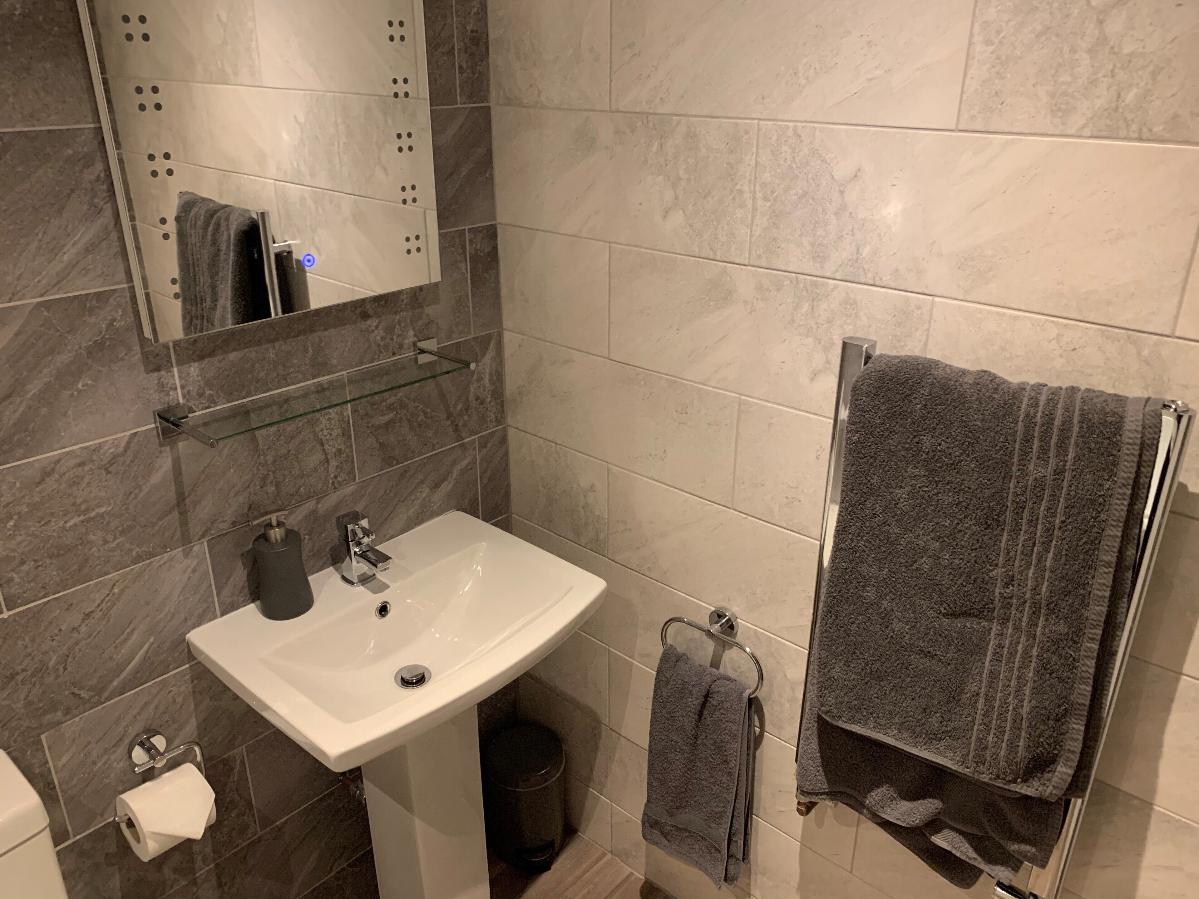 Ein Badezimmer mit einem weißen Waschbecken, einem Spiegel, einer Glasablage und einem Handtuchhalter.