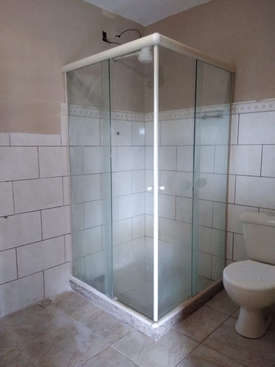A bathroom with a glass-enclosed shower, a toilet, and tiled walls.