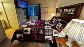 Una camera da letto con un letto grande, una TV fissata al muro, una finestra con tende e un comodino con una lampada.