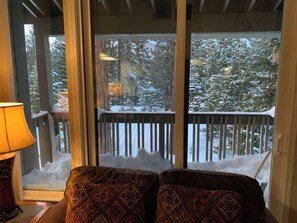 Ein gemütliches Zimmer mit Blick auf einen verschneiten Wald durch große Fenster.