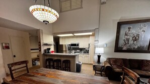 Un'area pranzo con tavolo e sedie in legno, una cucina sullo sfondo e un quadro appeso al muro.