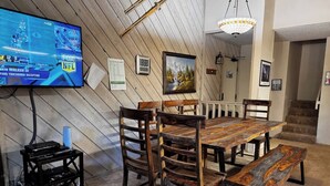 Un'area pranzo con un tavolo e sedie in legno, una televisione fissata alla parete e una scala sullo sfondo.