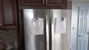 A stainless steel refrigerator with two doors, a wooden cabinet above it, and a clock on the wall. - Entertainment 4539 (Snellville)