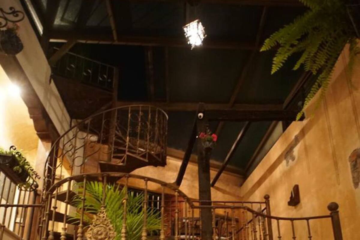 Een stenen trap met ijzeren hekwerk, die leidt naar een balkon met uitzicht op het interieur.