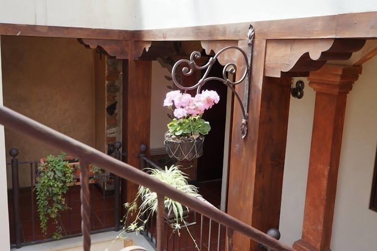 Een balkon met een smeedijzeren hekwerk, een houten deur en bloeiende hangmanden.