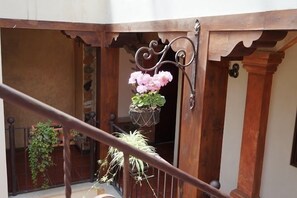 Een balkon met een smeedijzeren hekwerk, een houten deur en bloeiende hangmanden.