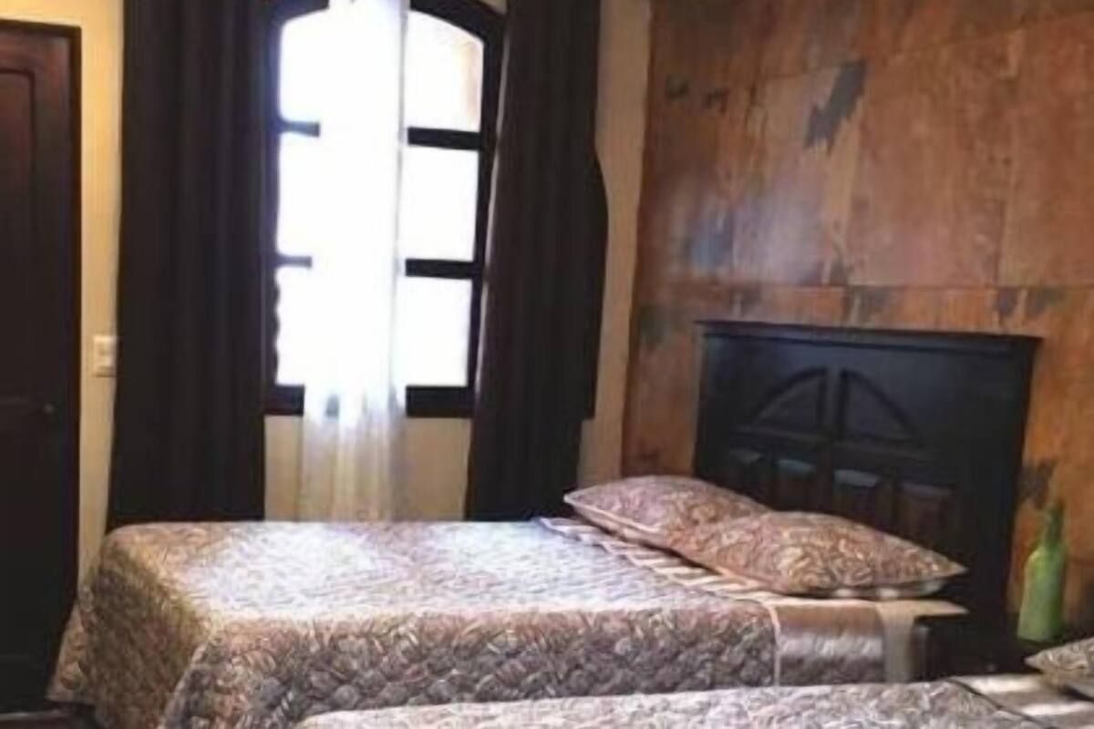 Een slaapkamer met een bed, een kroonluchter, een open haard en een groot raam met gordijnen.