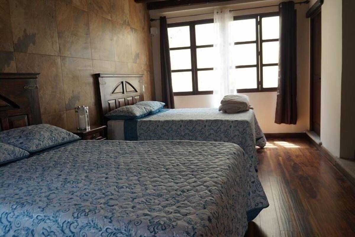 Slaapkamer met twee bedden, houten vloer, een raam met gordijnen en een hoofdeinde.