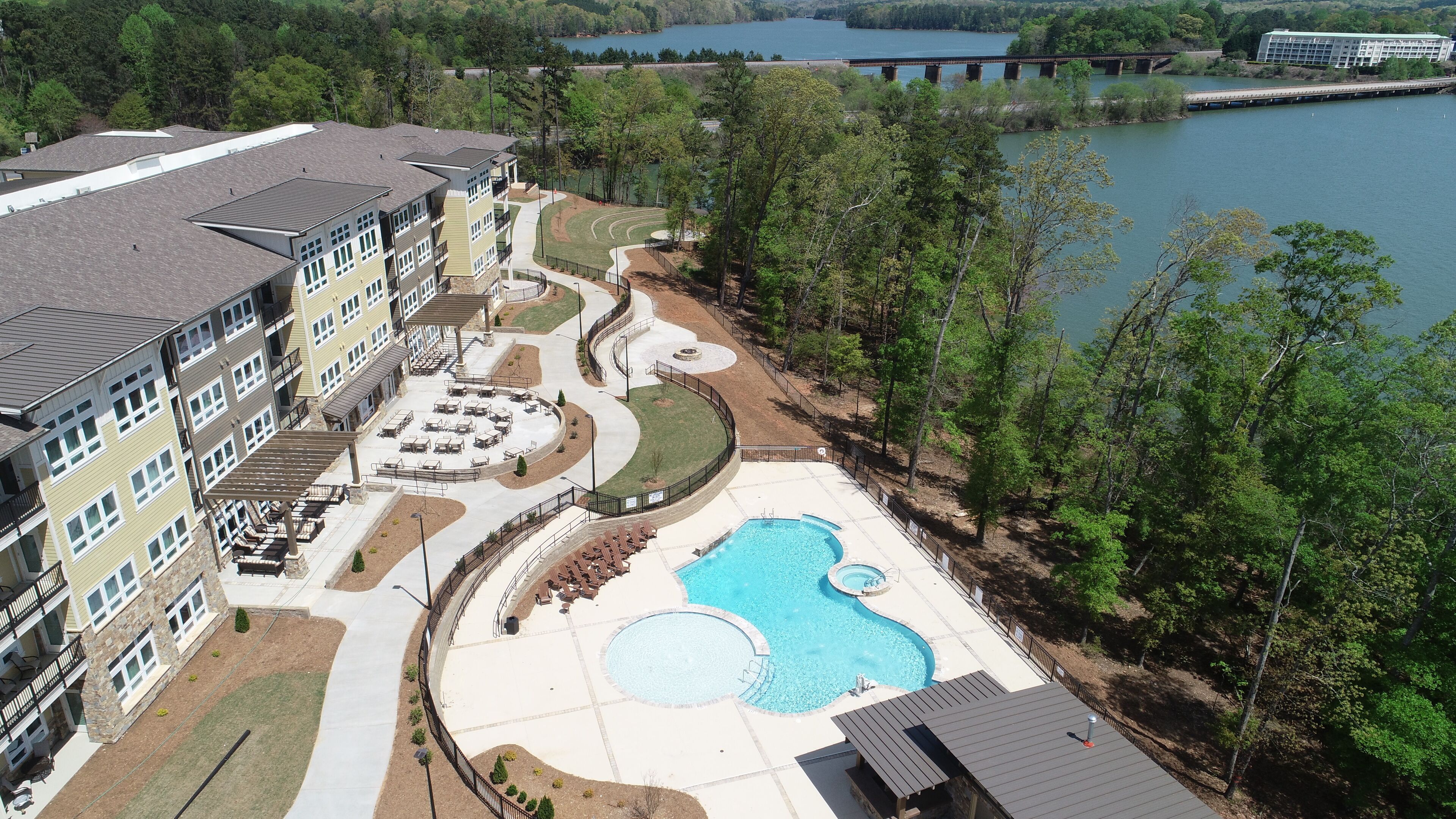 A multi-story hotel with a pool area, including a large pool and a smaller circular pool, surrounded by a walking path and outdoor seating.