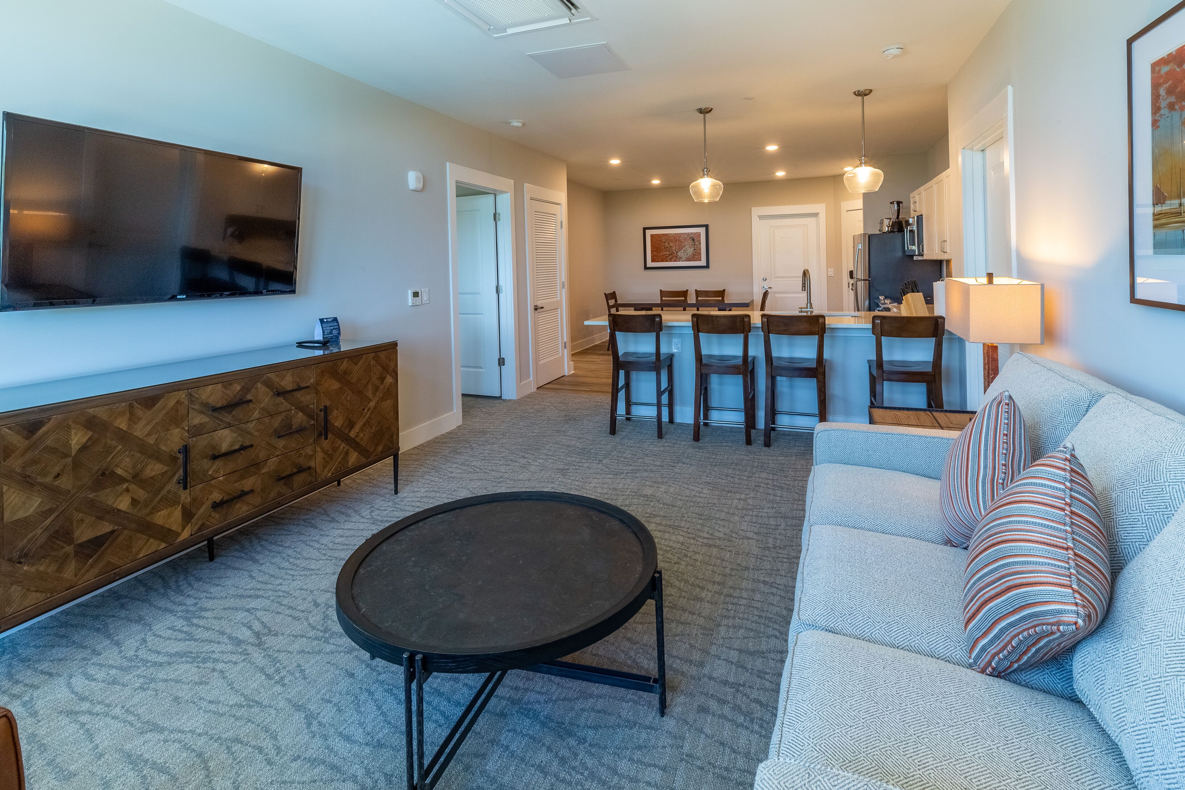 A modern living room with a sofa, coffee table, and TV. There is a kitchen area with a dining table and chairs.