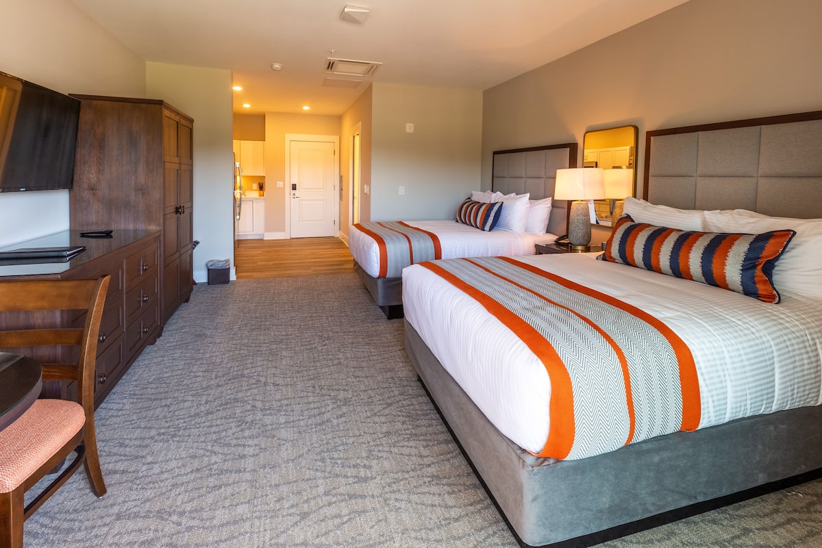 A hotel room with two beds, a desk, and a chair.