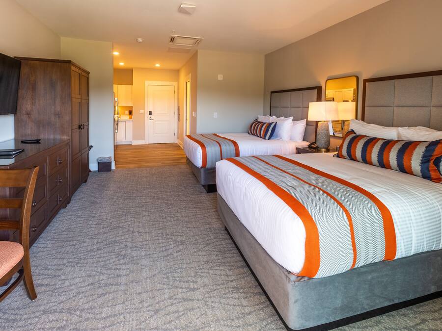 A hotel room with two beds, a desk, and a chair.
