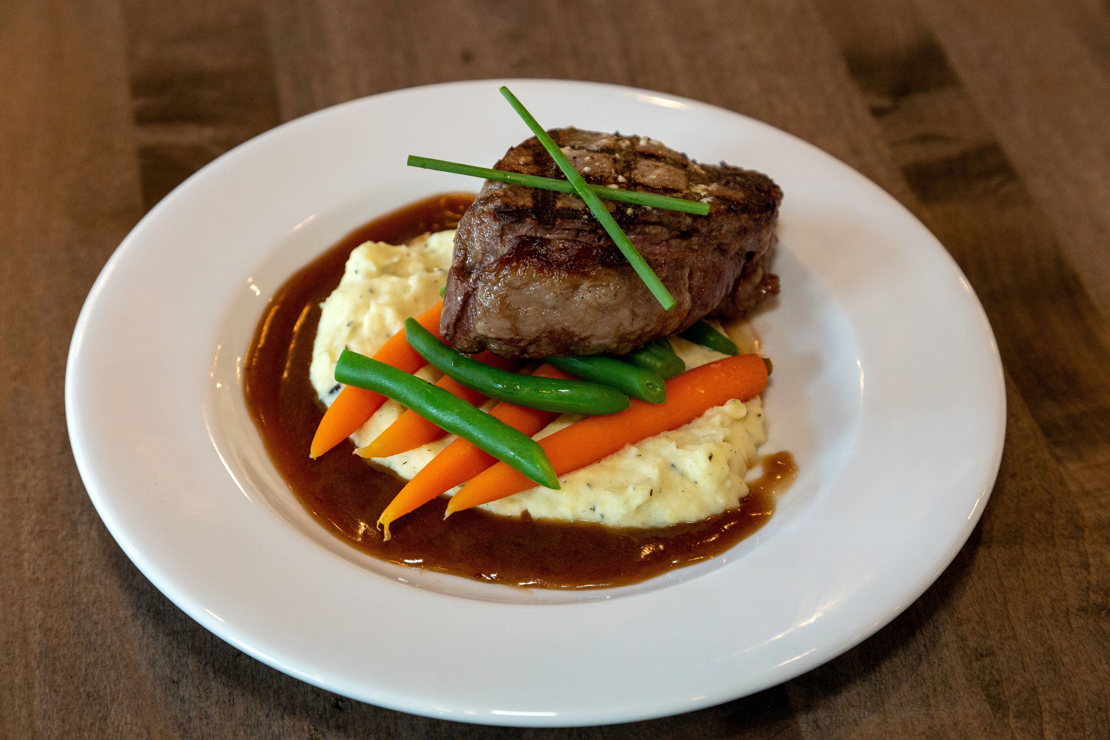 A plate with a steak, mashed potatoes, carrots, and green beans.