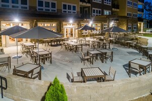 Un patio al aire libre con varias mesas y sillas, algunas con sombrillas, y un muro de piedra en primer plano.