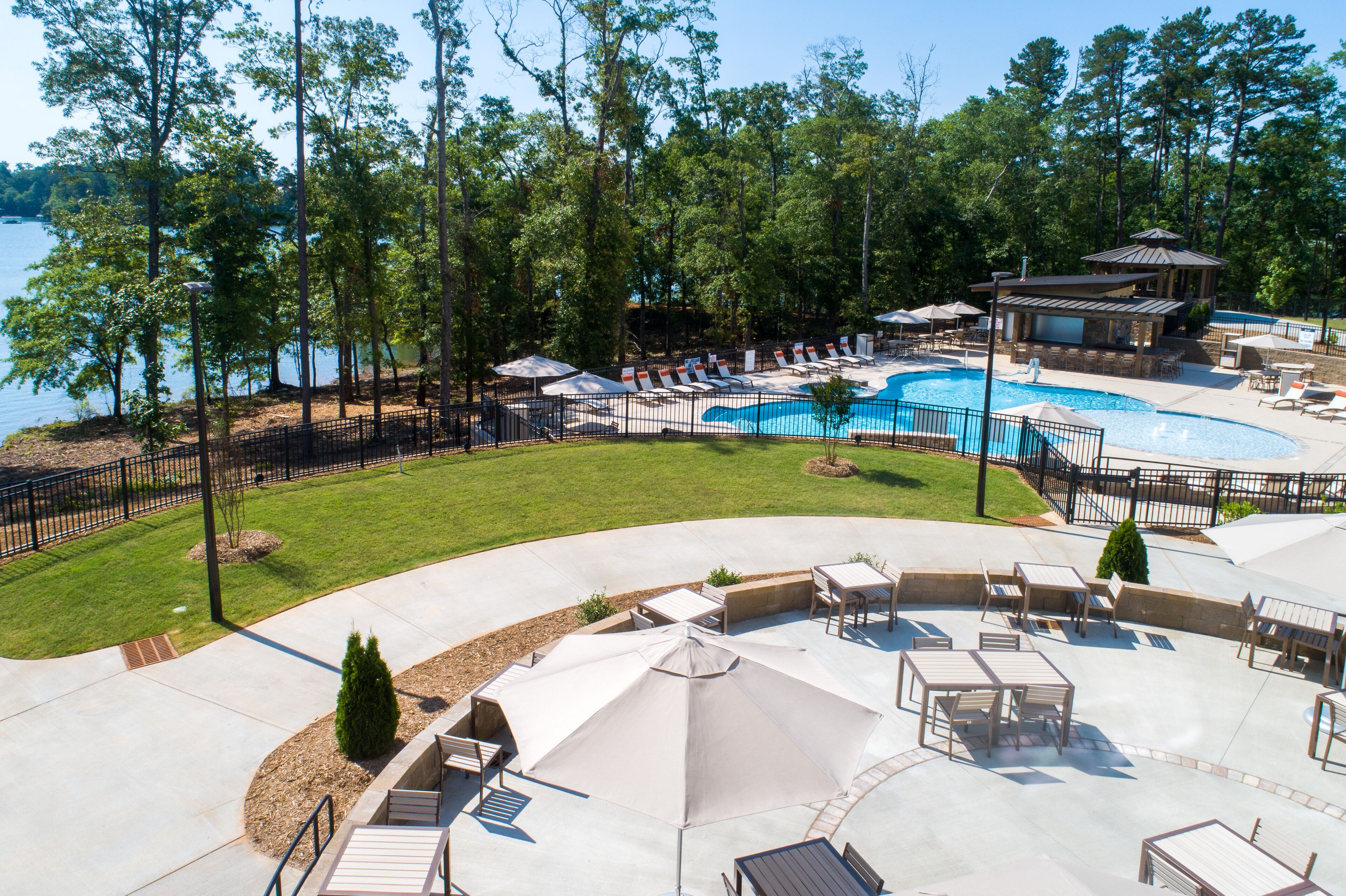 A pool area with lounge chairs and umbrellas, surrounded by a fence and trees.