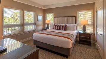 A bedroom with a large bed, two bedside tables with lamps, and windows with blinds.