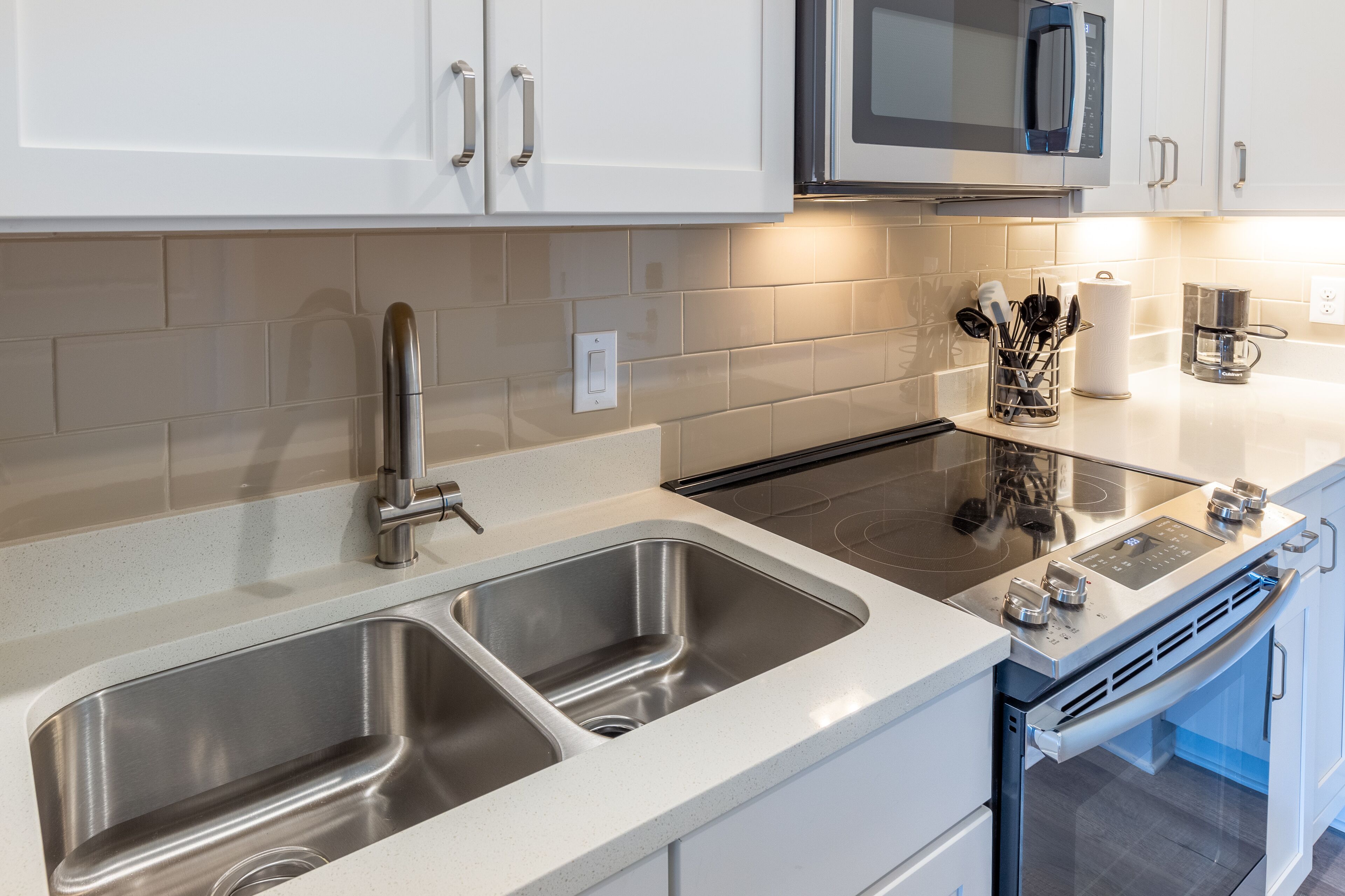 Una cocina moderna con electrodomésticos de acero inoxidable, un lavamanos doble y armarios blancos.