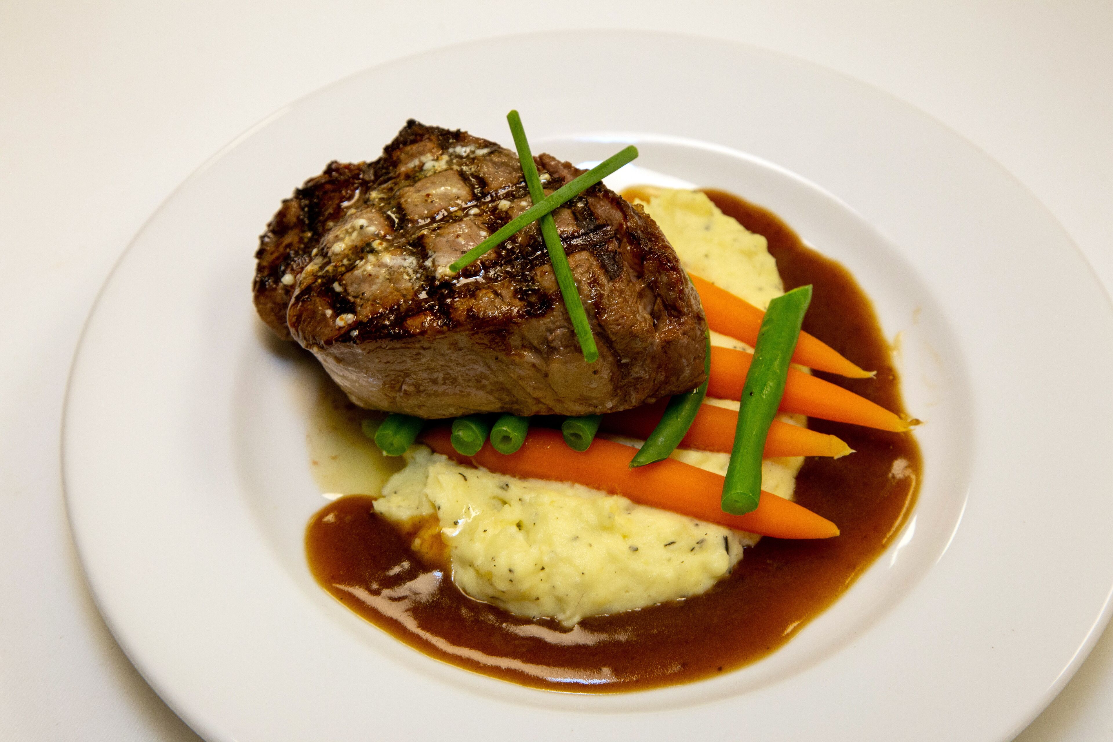 A plate with a piece of meat, mashed potatoes, carrots, and green beans.