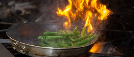 A pan on a stove with green vegetables and flames.