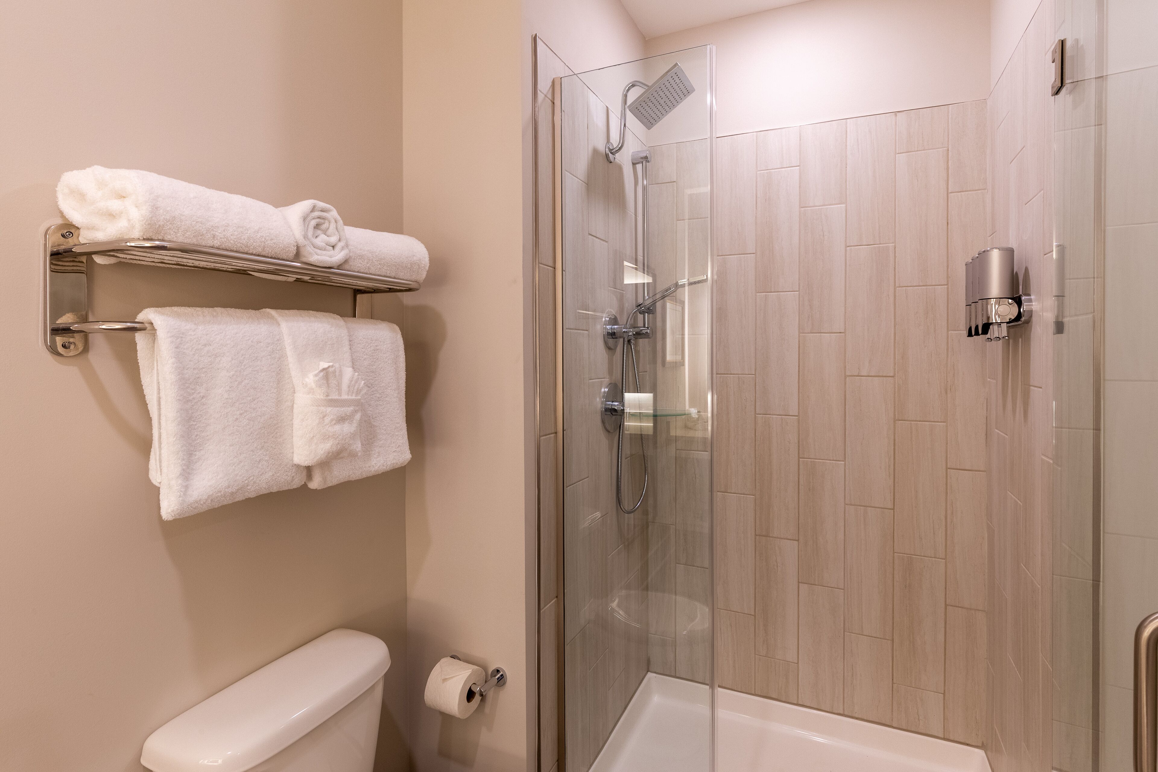 A modern bathroom with a glass-enclosed shower, a toilet, and a towel rack with neatly folded towels.